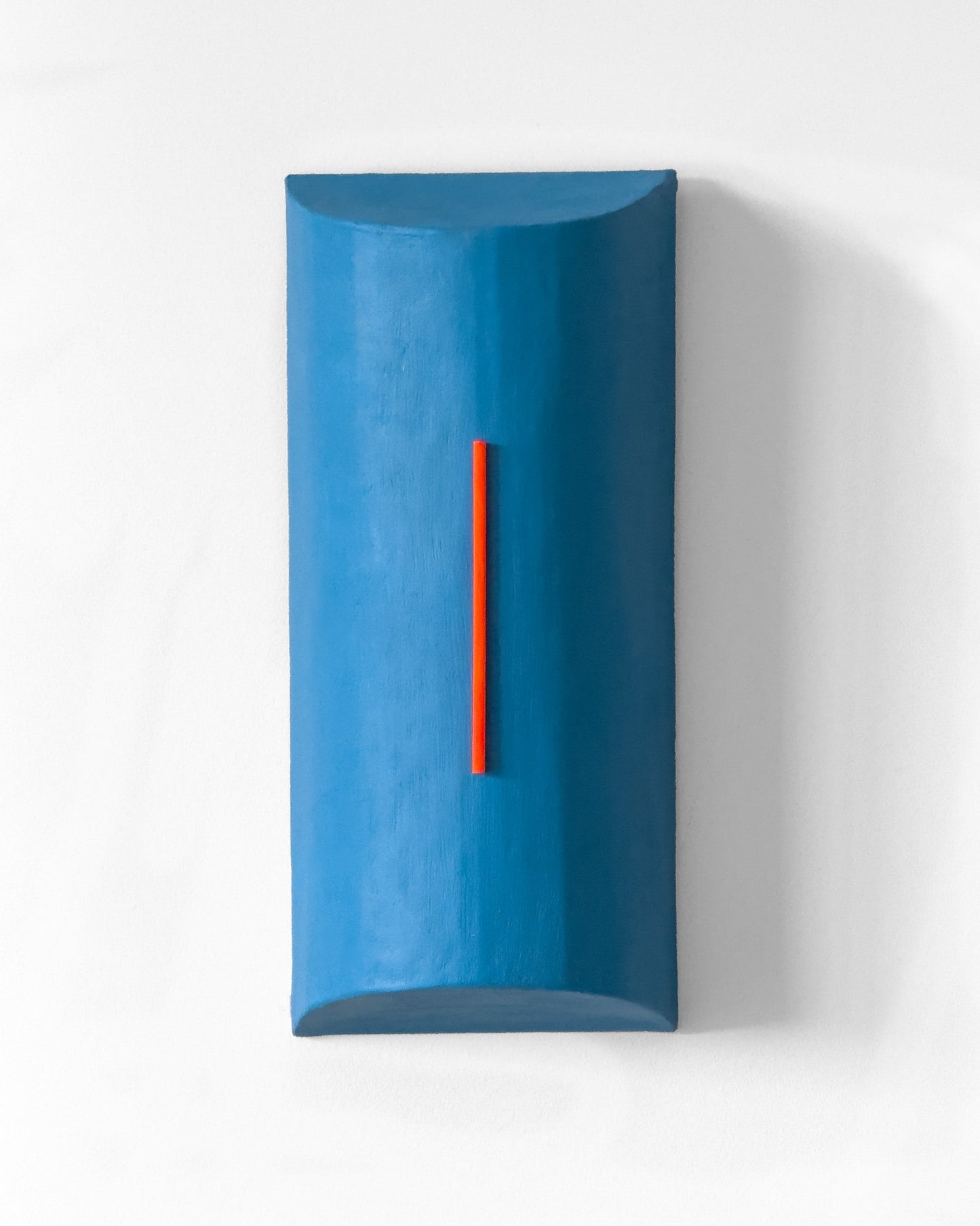 A minimalist, geometric blue wall sculpture with a vertical red-orange accent by Olshbau, mounted on a white wall.