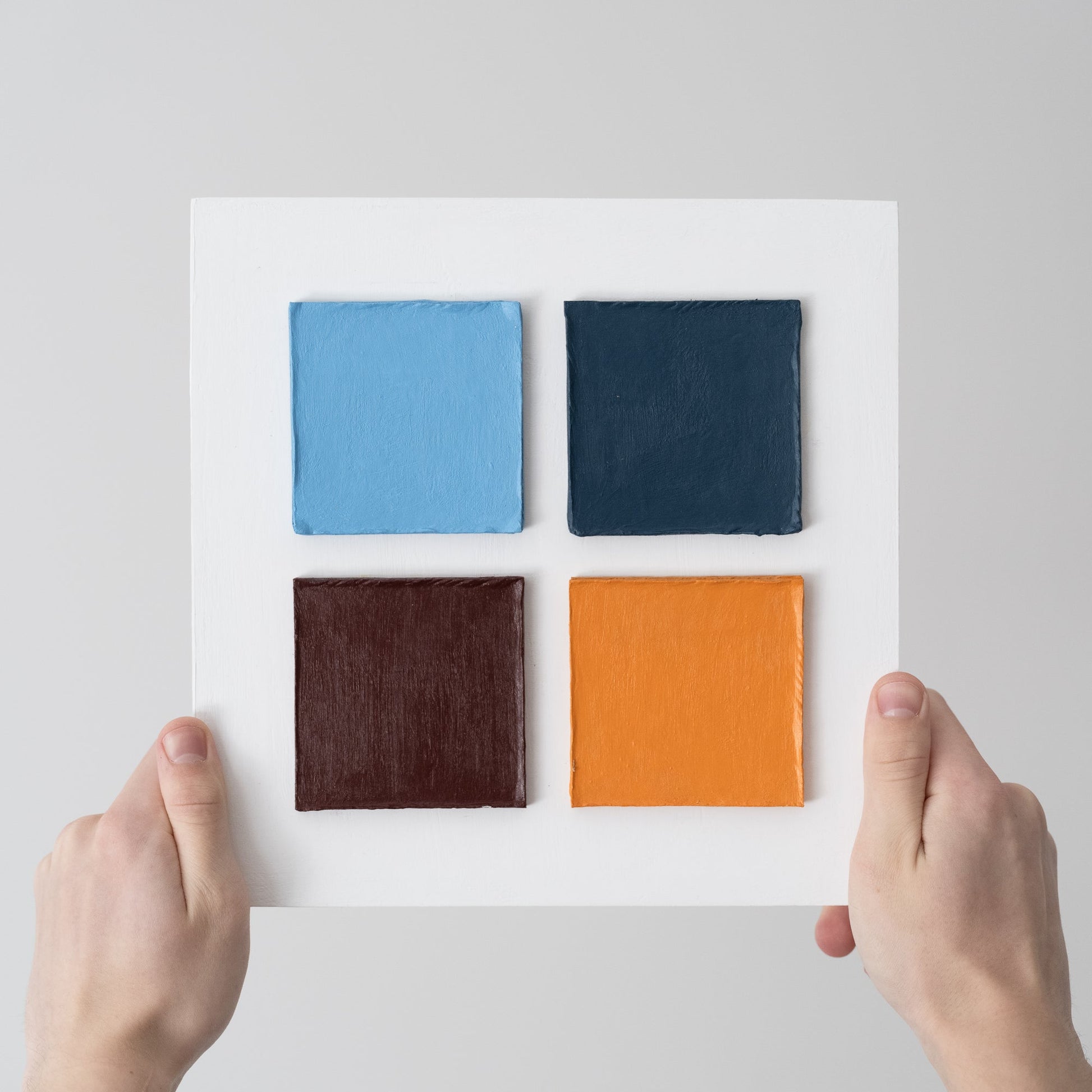 Hands holding a wallart Four Squares in Exile – Textured Cardboard on Plywood 25 by 25 cm