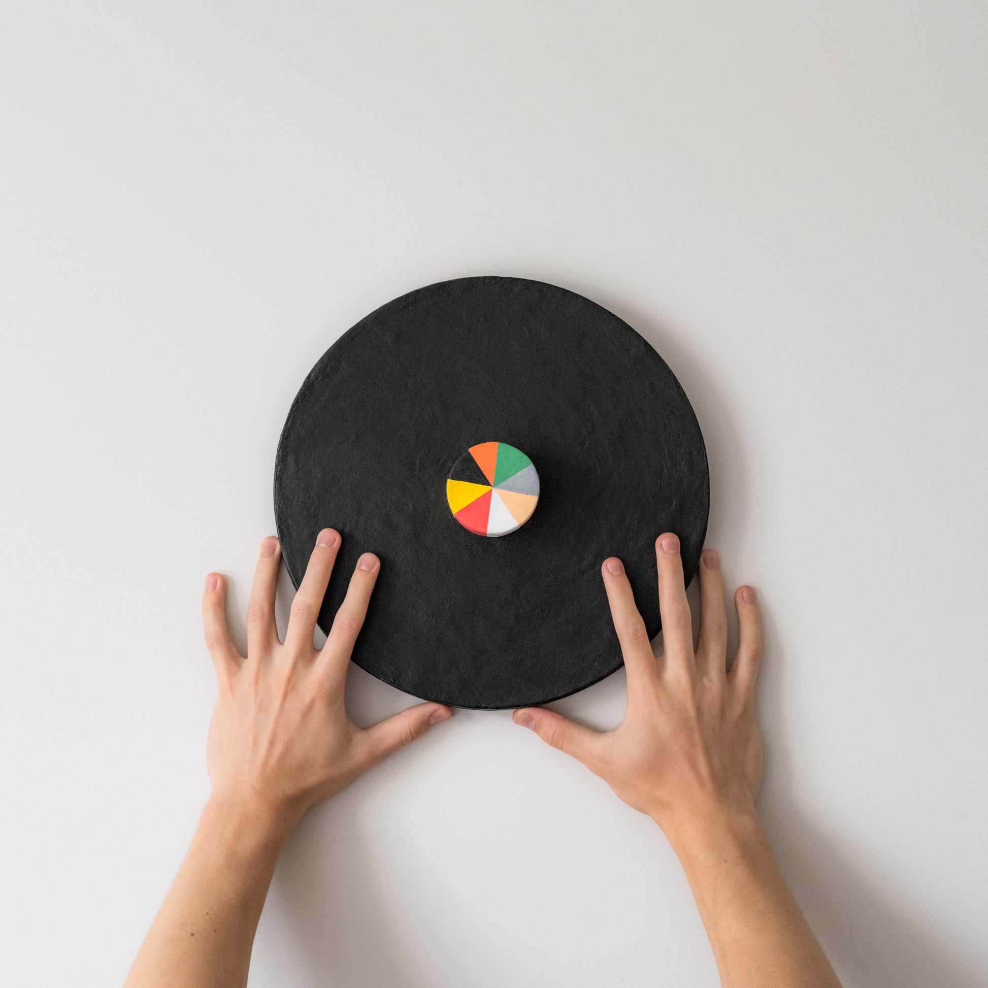 Hands positioning a Suprematist-inspired Olshbau wall sculpture—black circular base with a vivid geometric core, echoing Malevich’s bold minimalism.