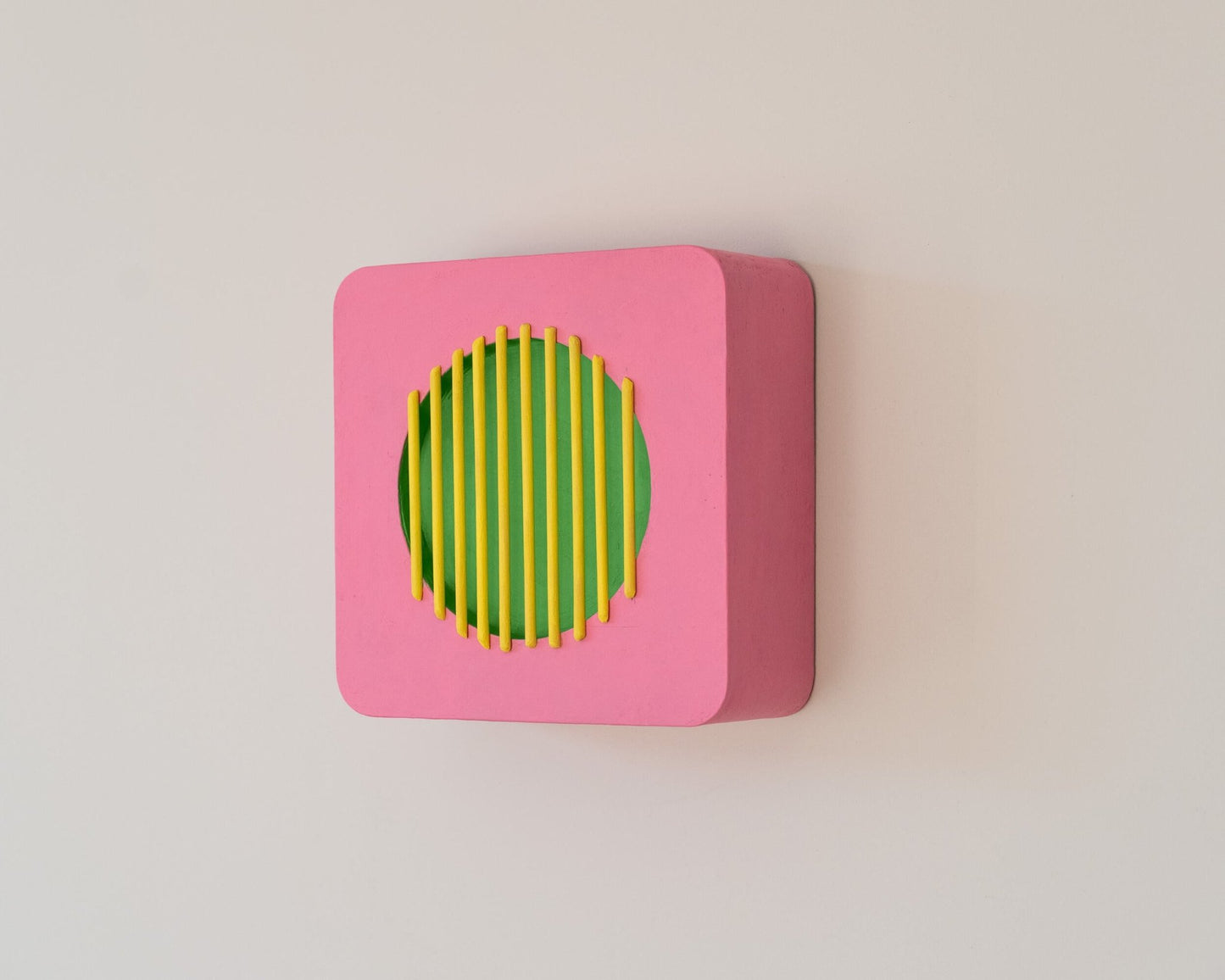 Modern wall sculpture in pink, green, and yellow with deep side profile, showing 3D geometric form inspired by vintage speaker design.