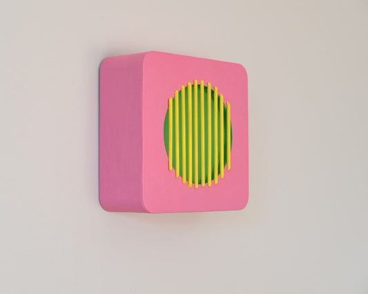 Side view of pink square wall sculpture with yellow vertical bars over a green circular center, inspired by vintage radios and modernist design.
