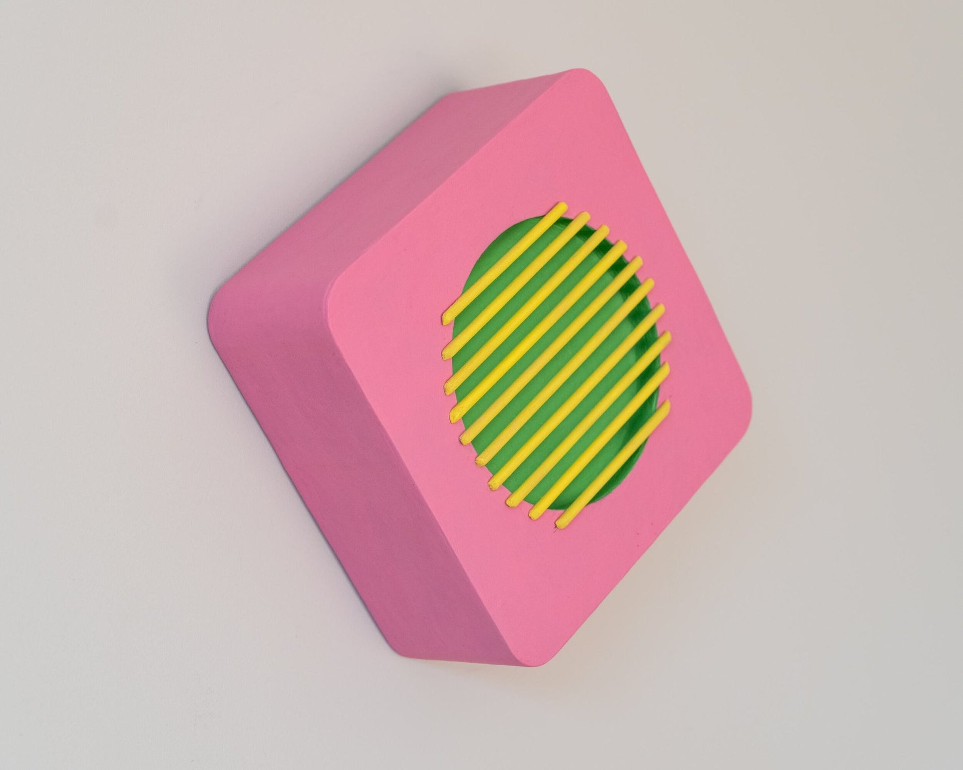 Rotated geometric wall sculpture in pink, green, and yellow with visible hanging point, showcasing 3D depth and bold modernist form.