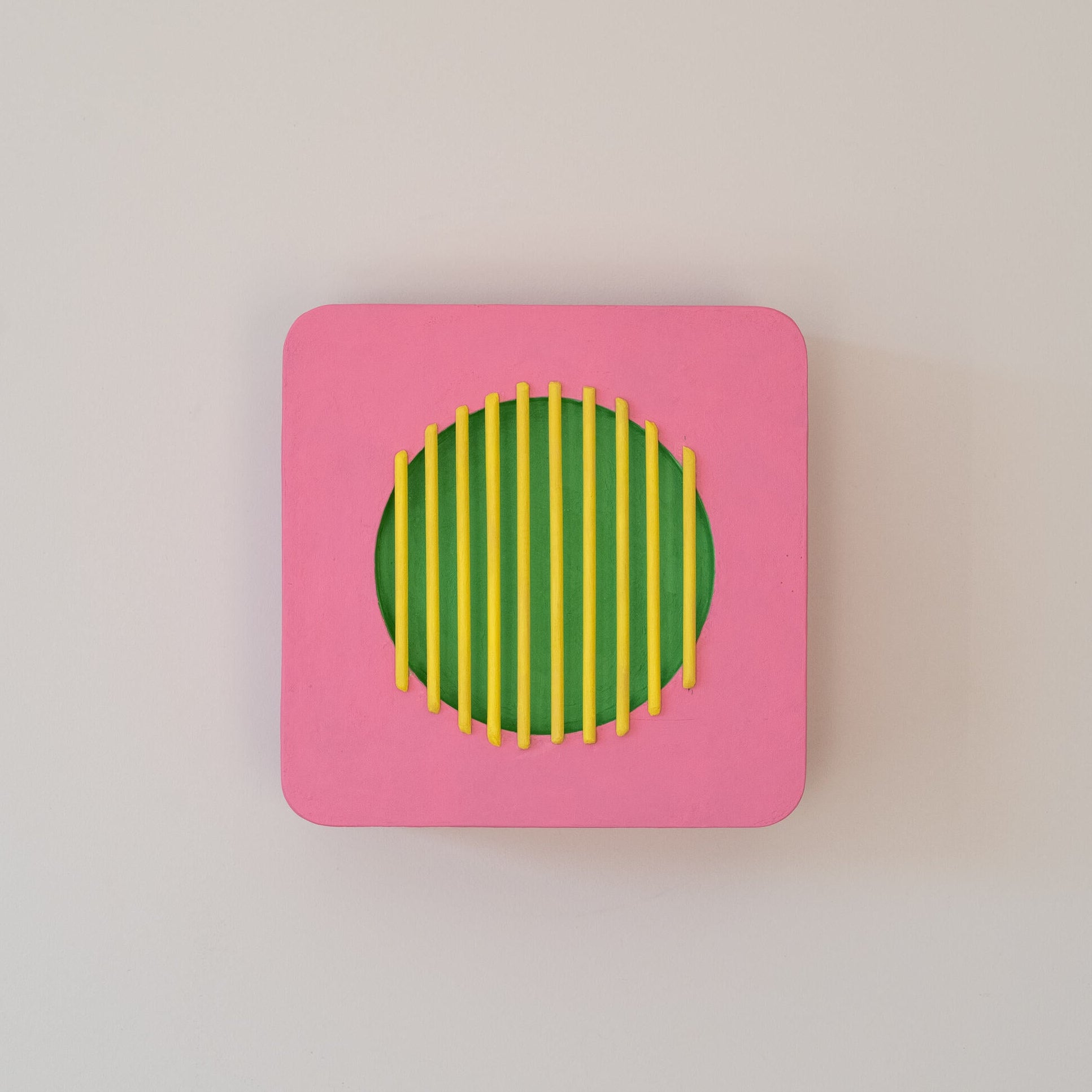 Abstract wall sculpture with pink square frame, green circular center, and yellow vertical bars,