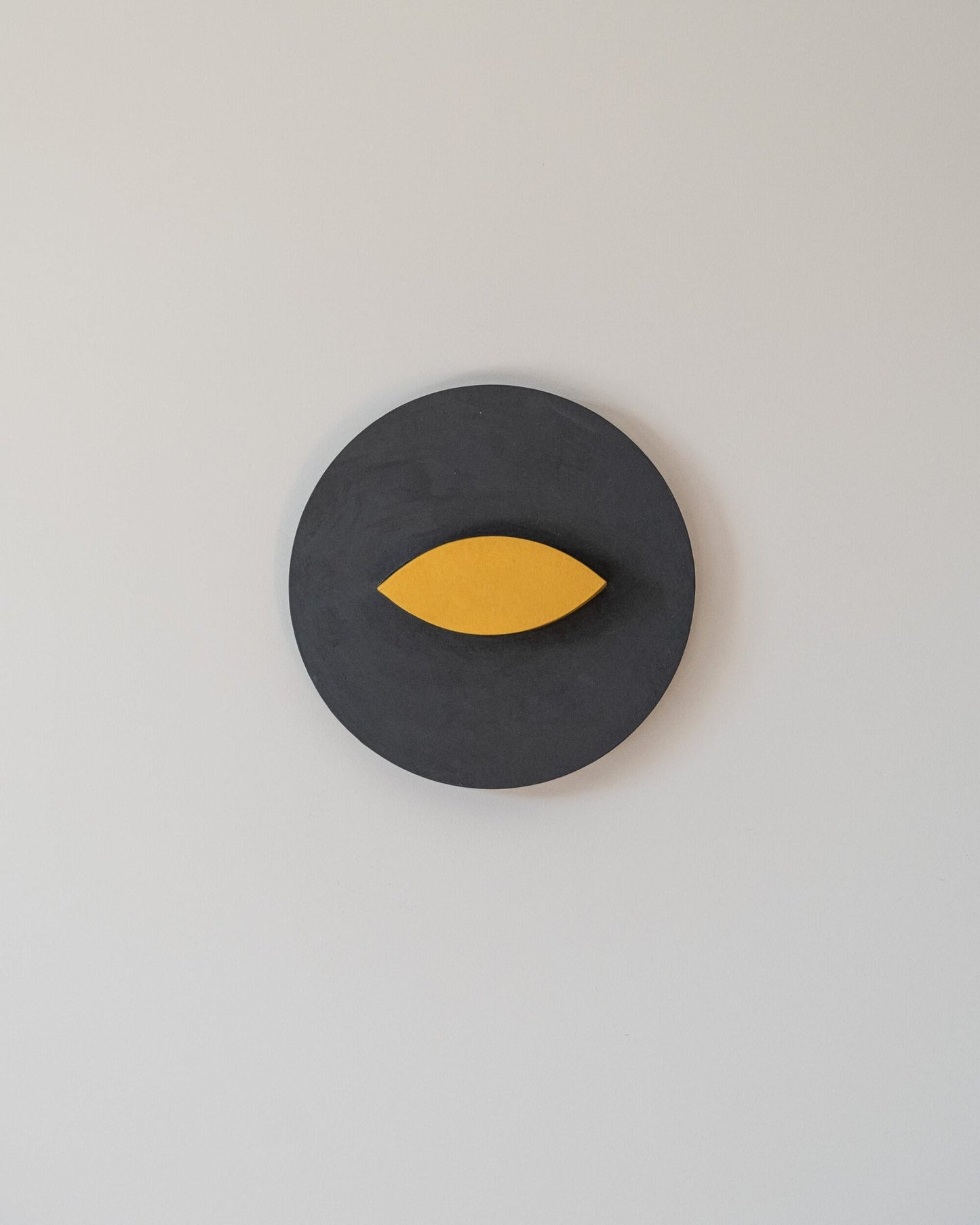Gray circular wall art object with a yellow leaf-like shape on a light gray background