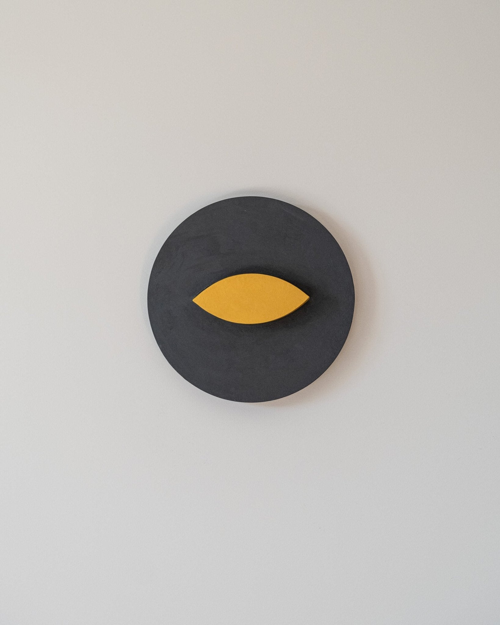 Gray circular wall art object with a yellow leaf-like shape on a light gray background