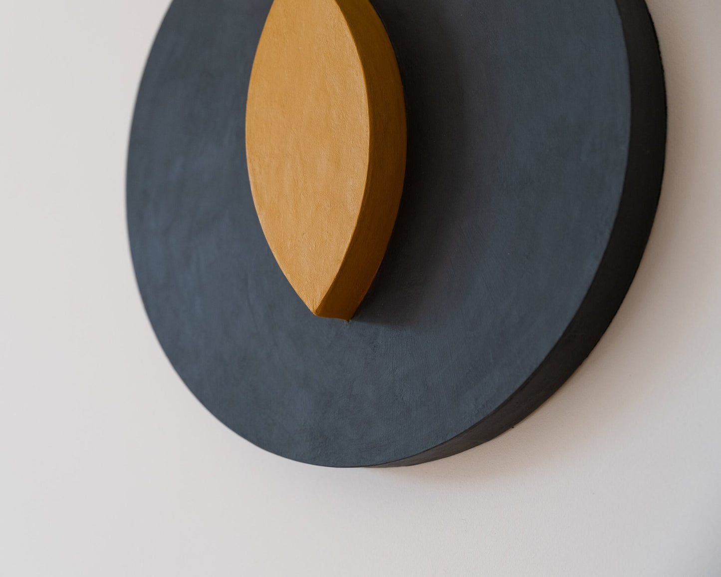 Close-up of a round wall art  in dark gray with a an vertical eye shaped element in the center. 
