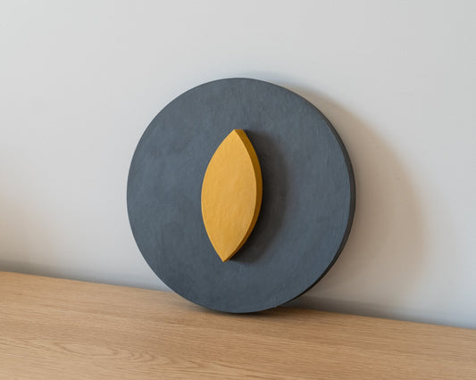 Decorative wall art piece with a yellow leaf on a dark gray circular base against a white wall. Handcrafted by Olshbau in Gdansk, Poland. Signed by the artist.