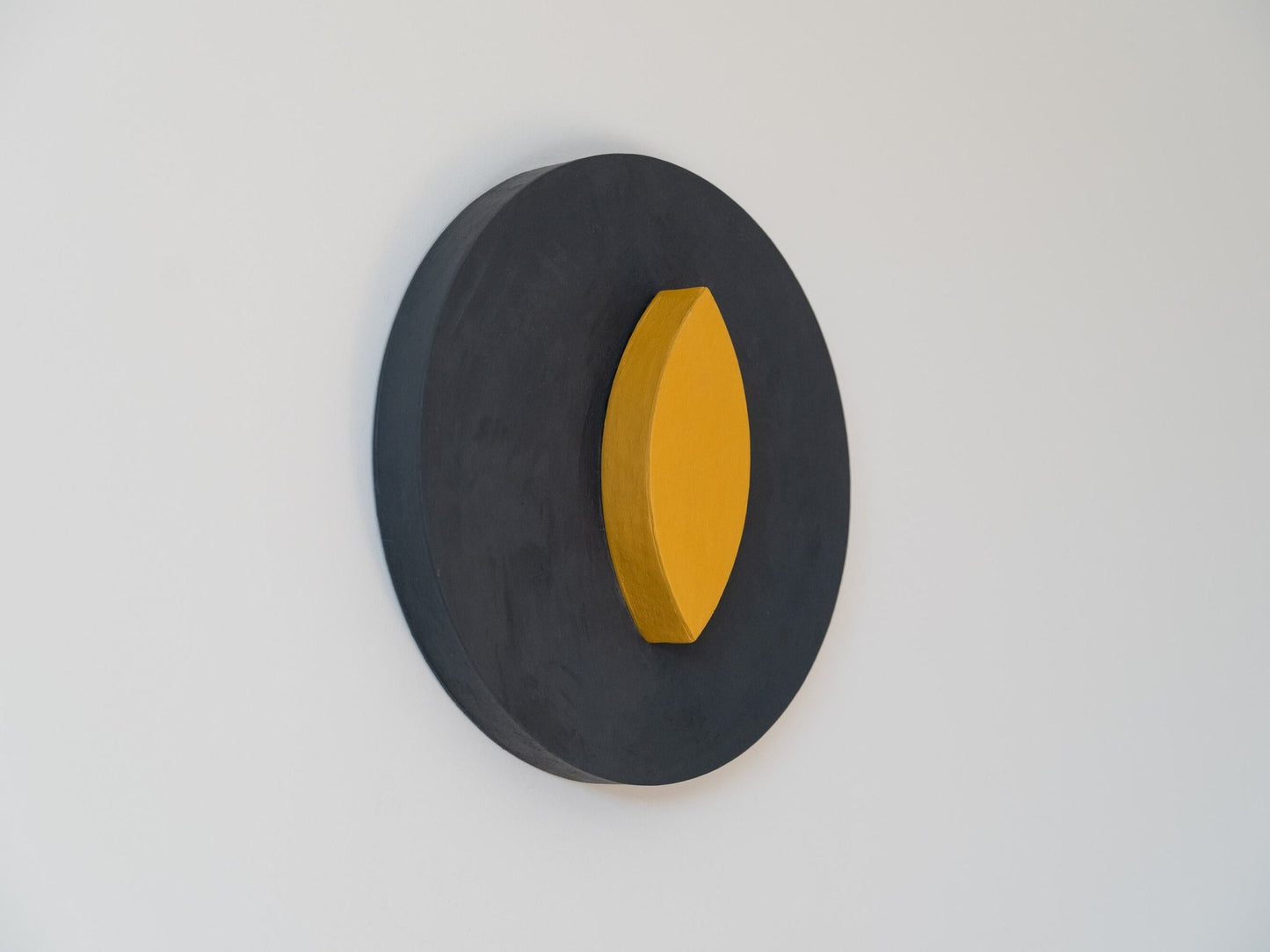 Black circular wall art with a yellow center on a gray background