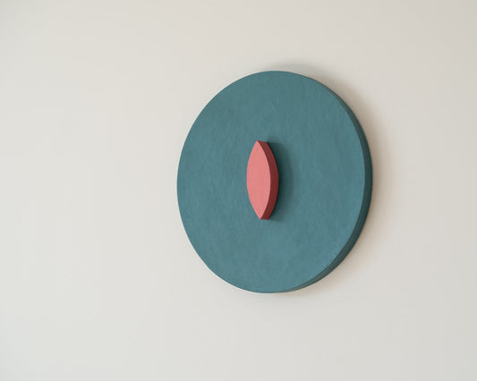 Teal circular wall art with a pink leaf-like shape in the center on a light gray background