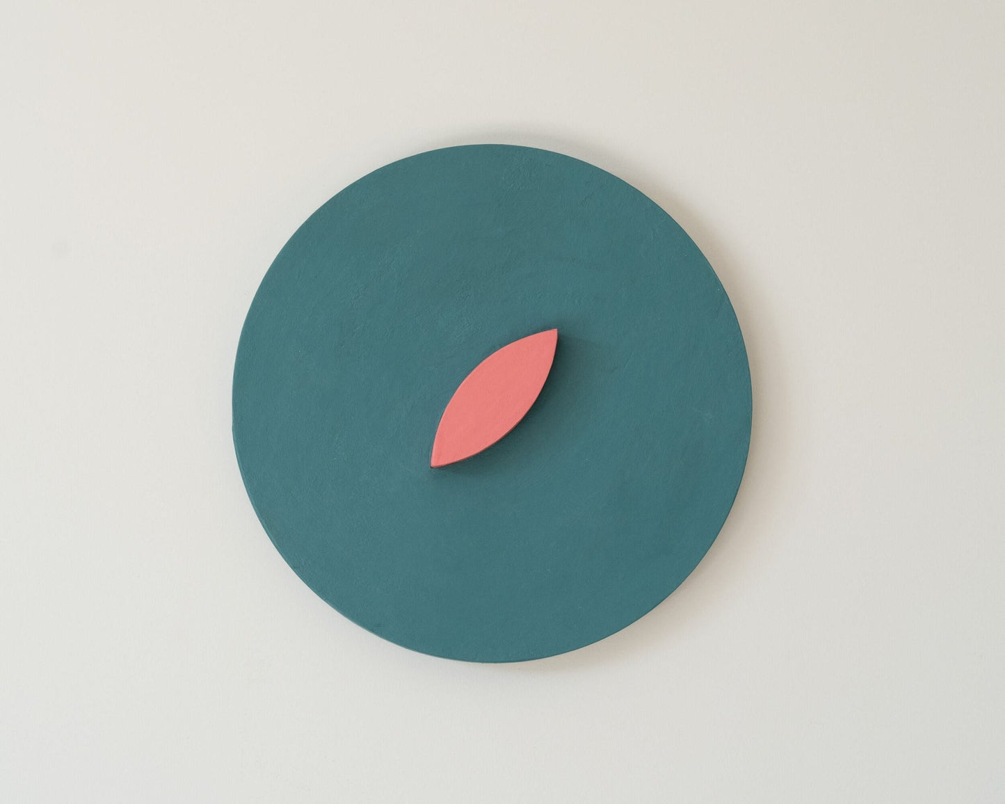 Teal circle with a pink leaf wall art on a light gray background