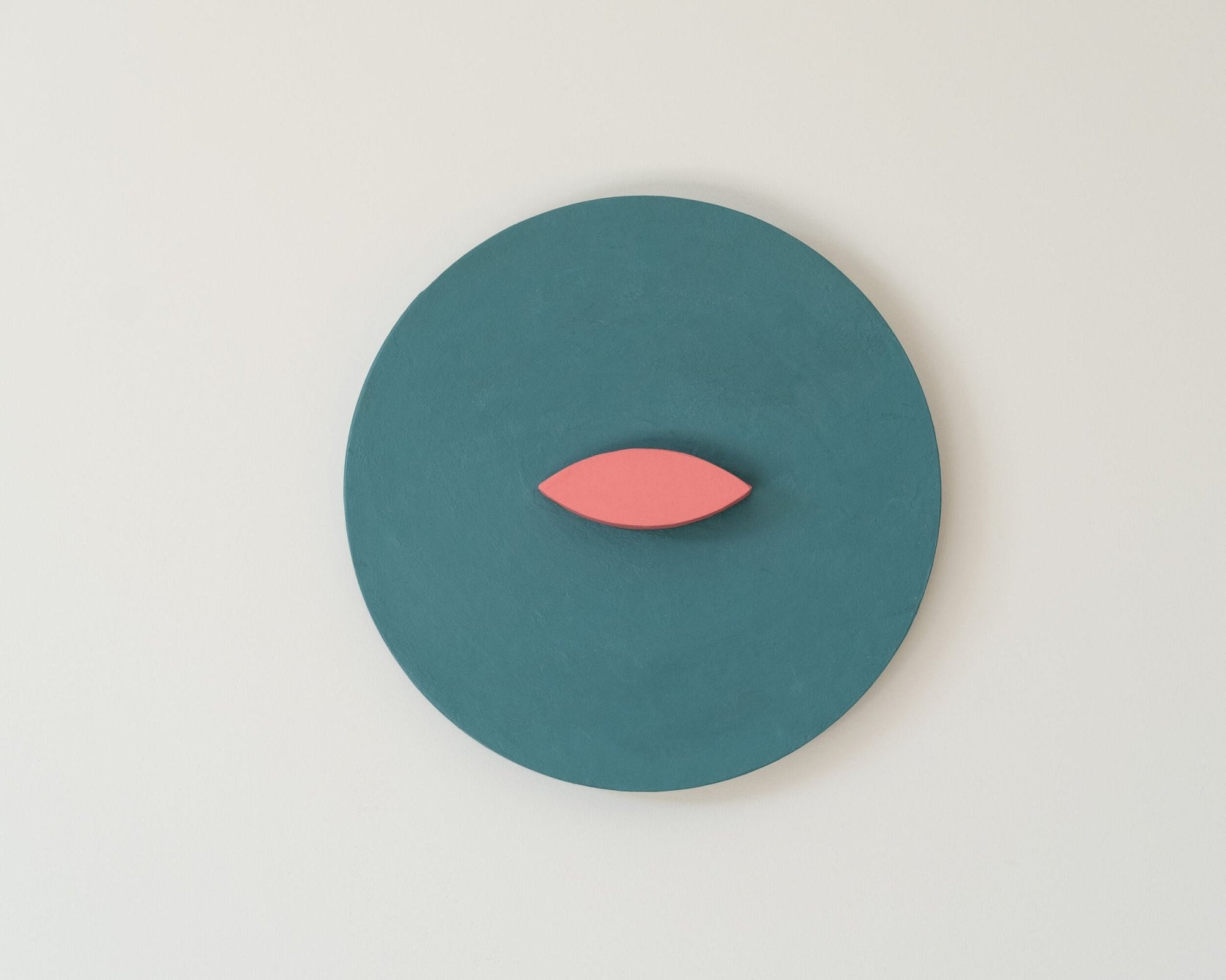 Teal circle with a pink leaf-like3D wall art ion a light gray wall