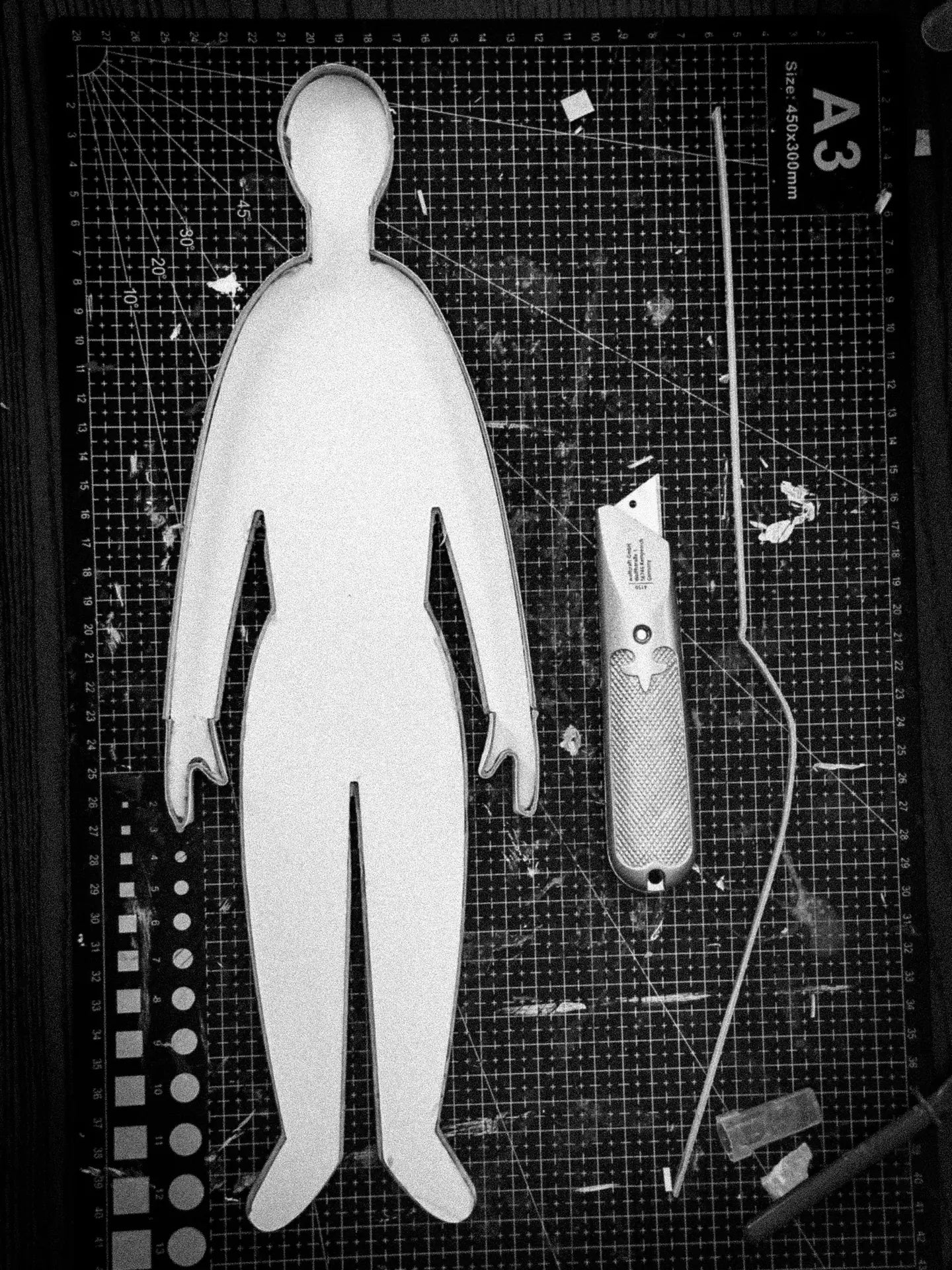 A standing figure cut from board on an A3 cutting mat, next to a utility knife