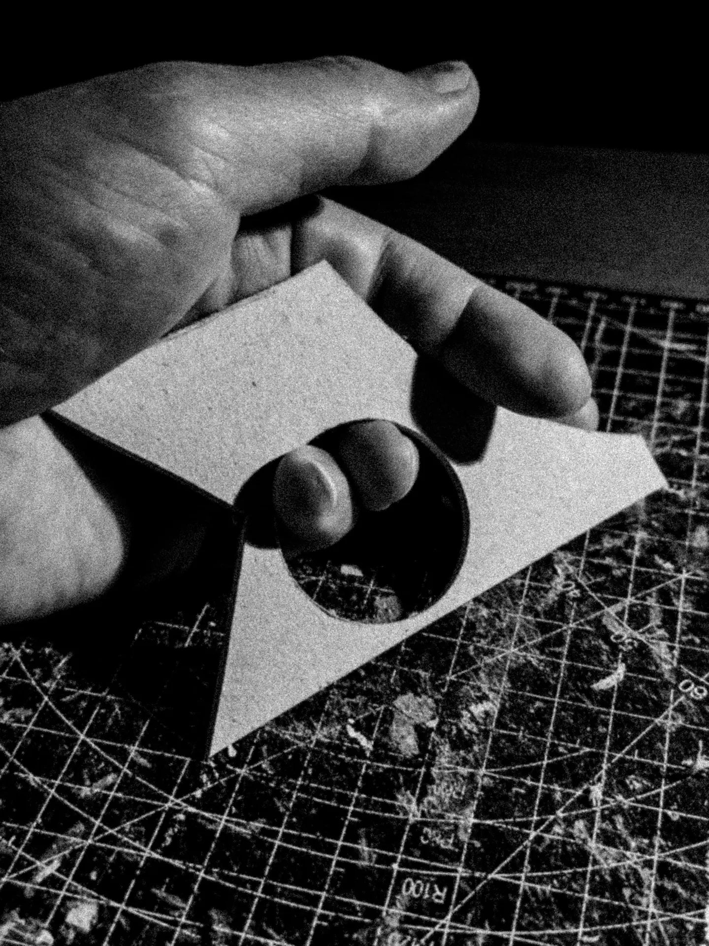 A hand holding a cardboard offcut with a round hole and a triangular point