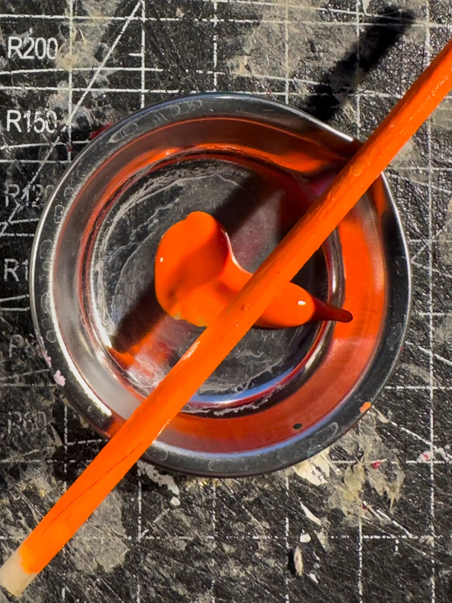 Orange acrylic paint in a glass dish with a brush across it, on a cutting mat
