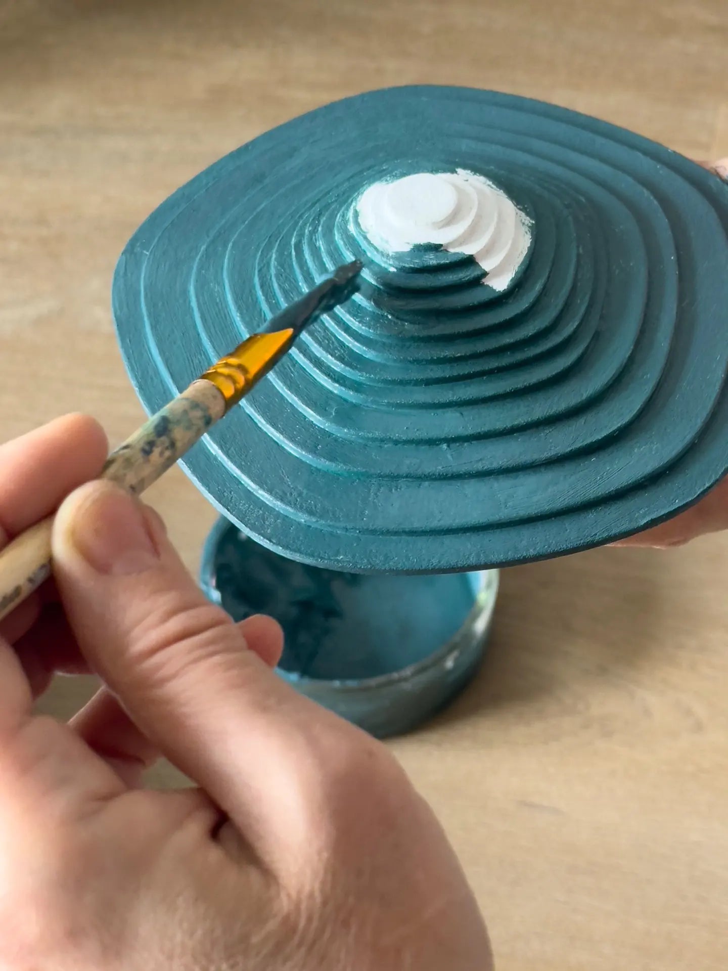 A fine brush painting the white centre of a teal stepped relief