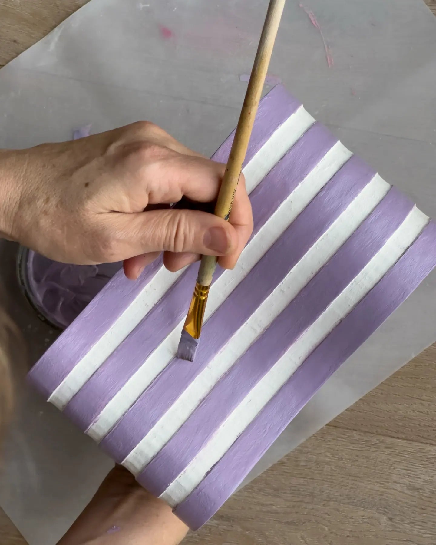 A hand painting purple stripes on a wavy white relief with a flat brush