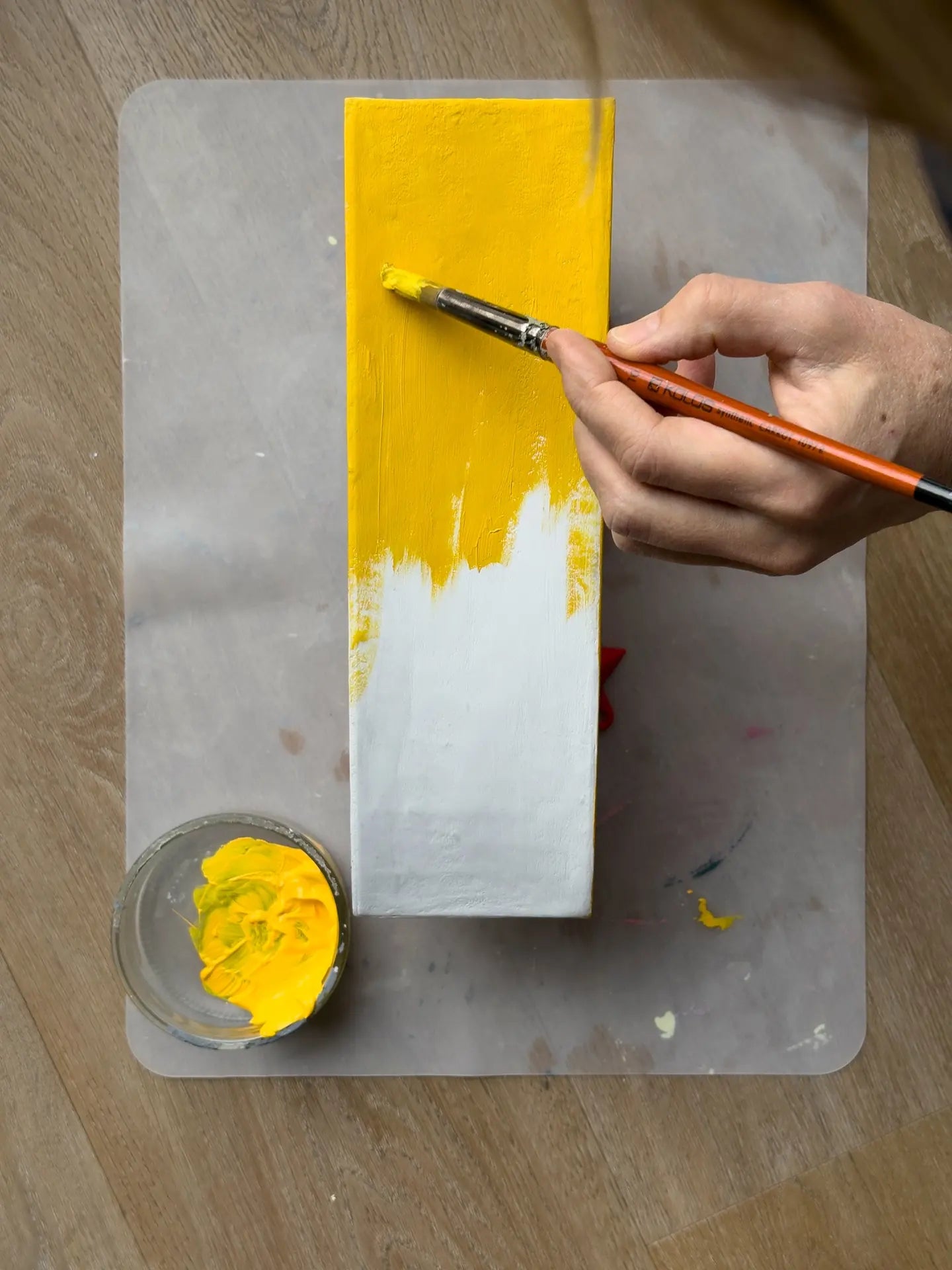 A hand painting a white block yellow with a brush, half finished