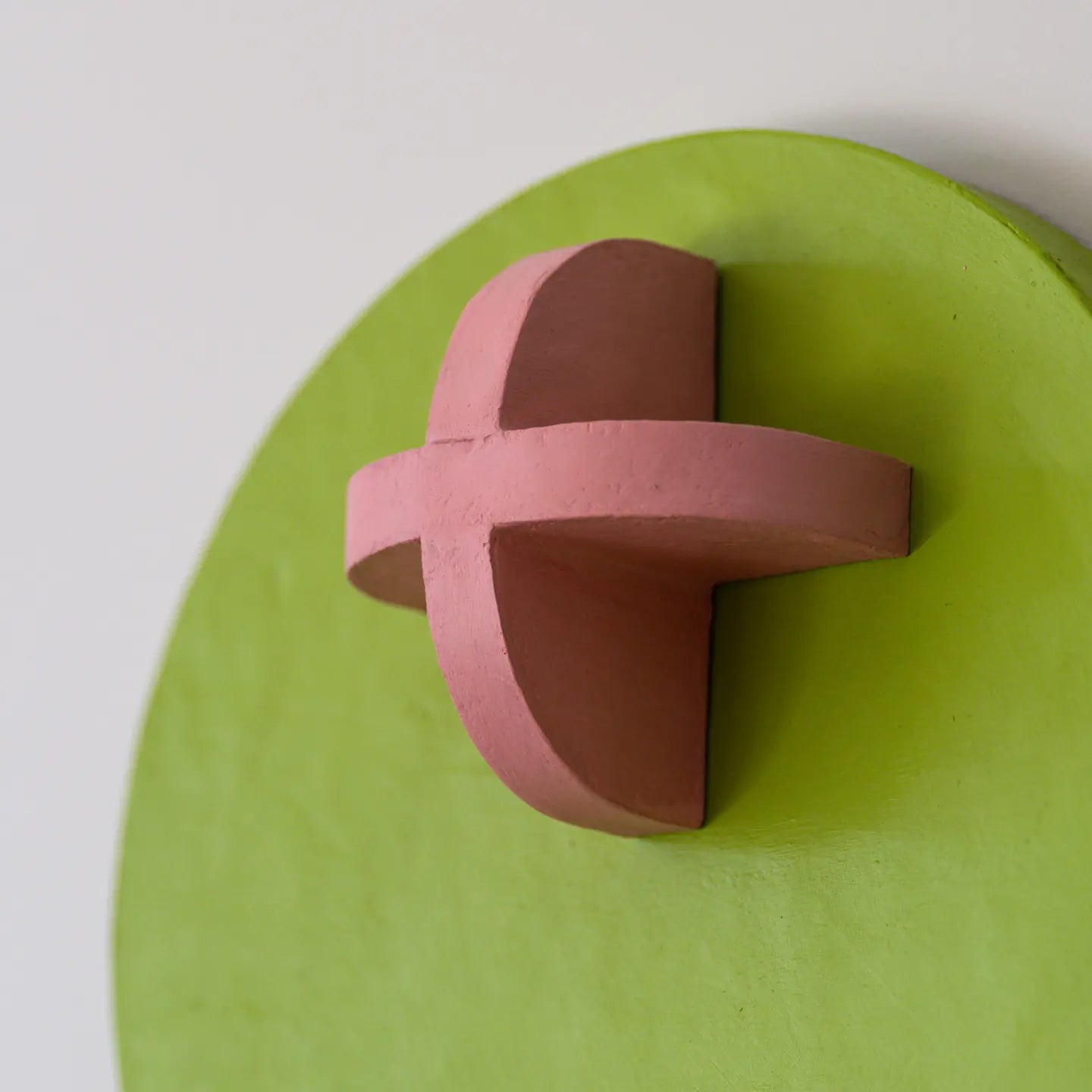 Close-up of a raised pink cross on a green disc, showing the depth of the relief