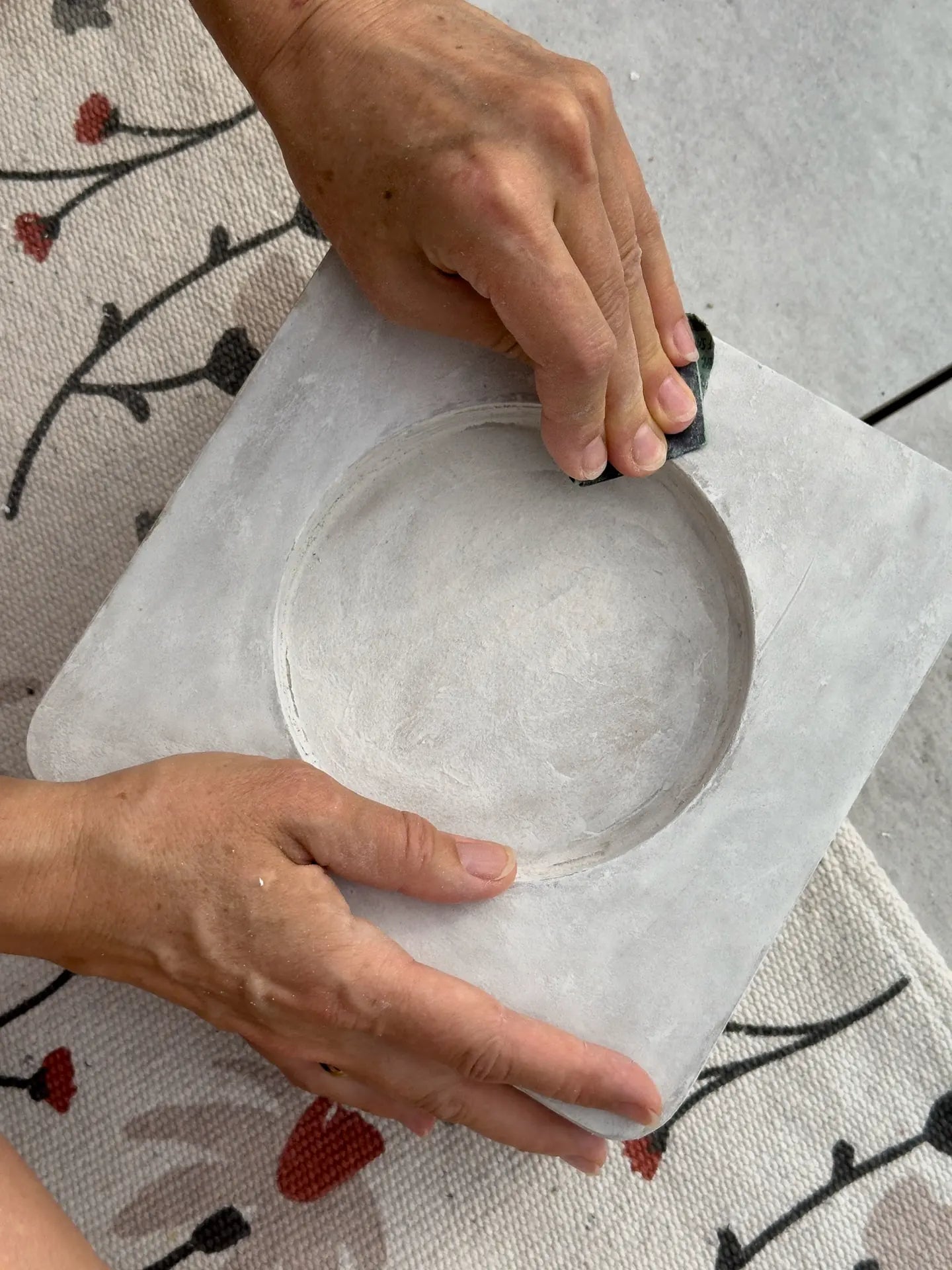 Two hands sanding the round recess of a grey coated relief with a sanding sponge