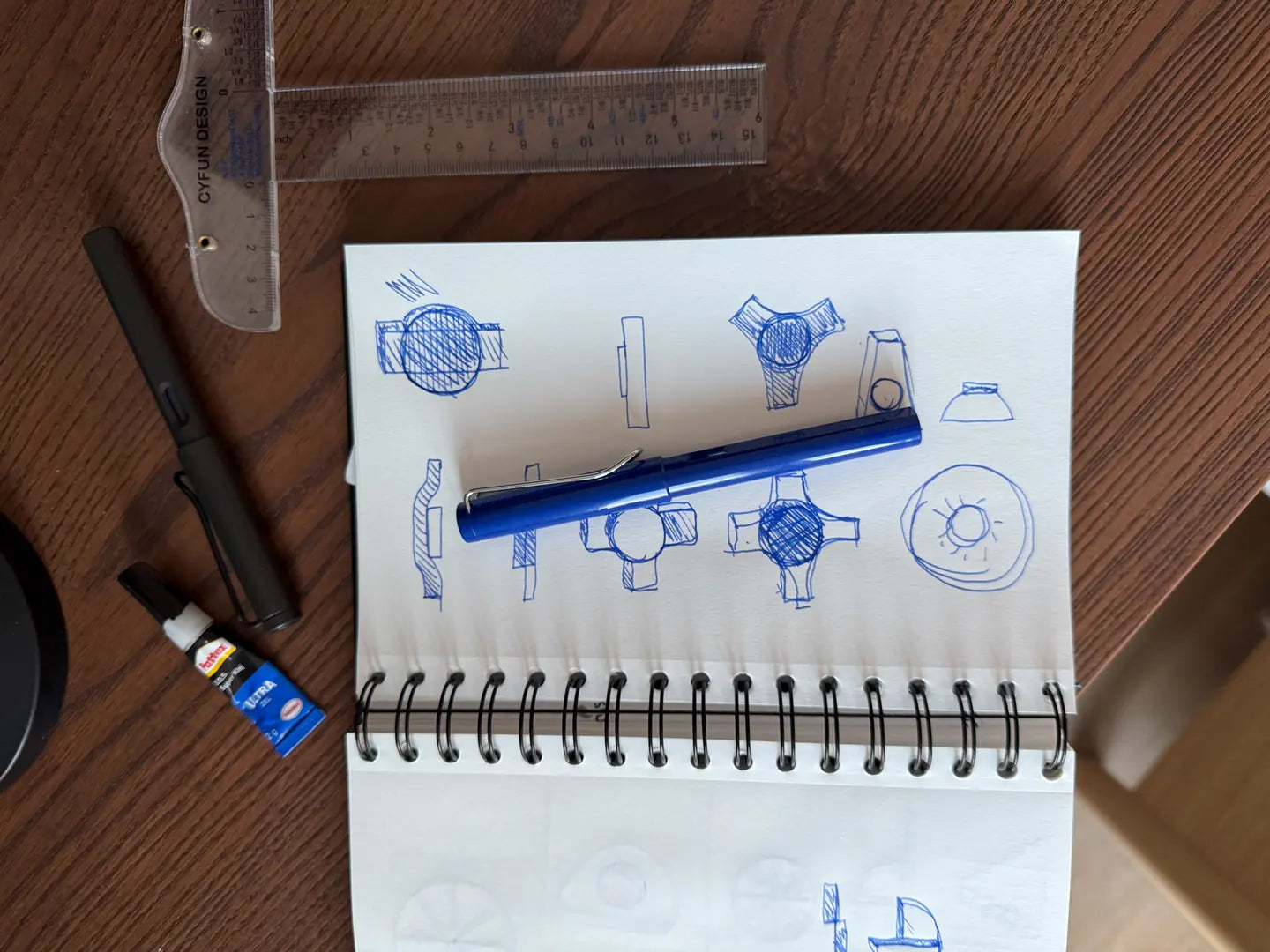 Sketchbook page with ballpoint drawings of an object from several sides, with rulers and a pen