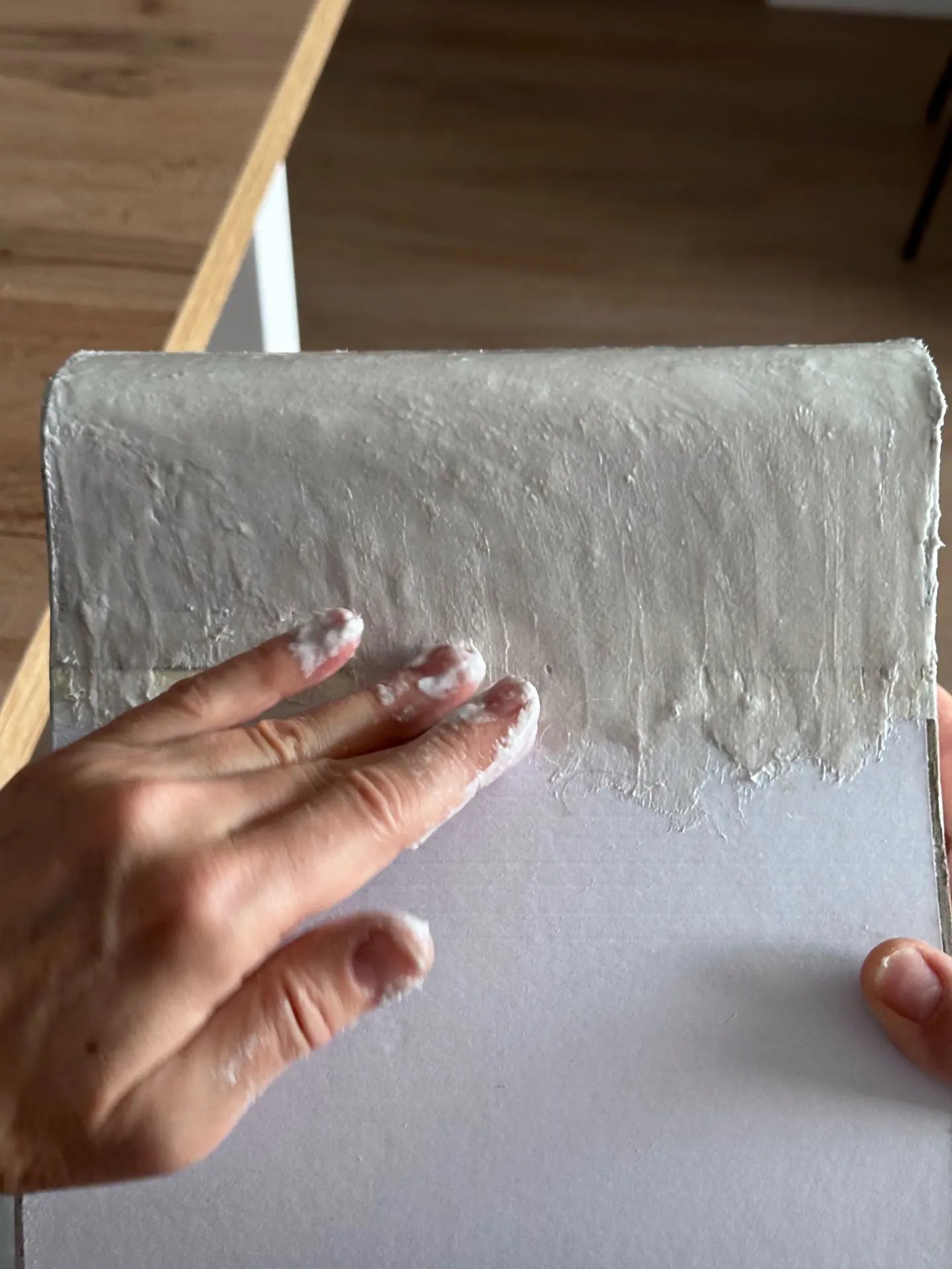 A hand spreading a grey textured coat over a curved cardboard form